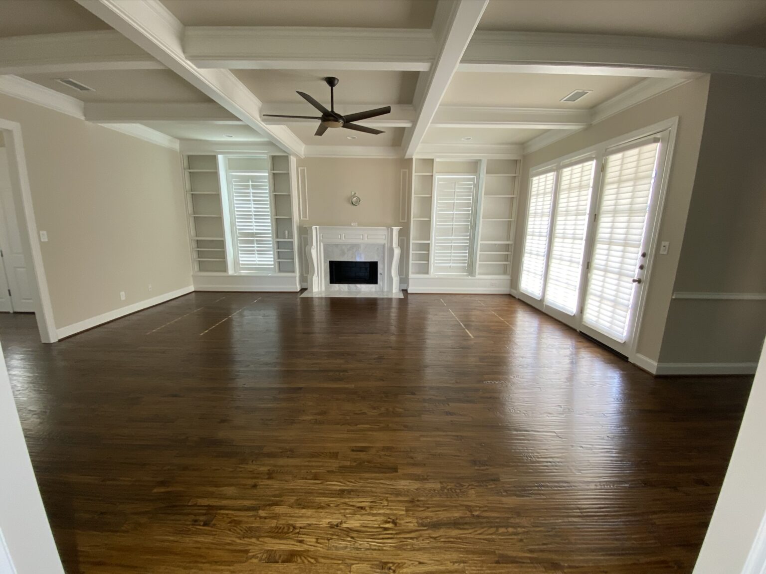 Spacious Plano living room with rich hardwood floors, natural light, and built-in shelving, showcasing the importance of proper hardwood floor maintenance in humid Texas seasons.