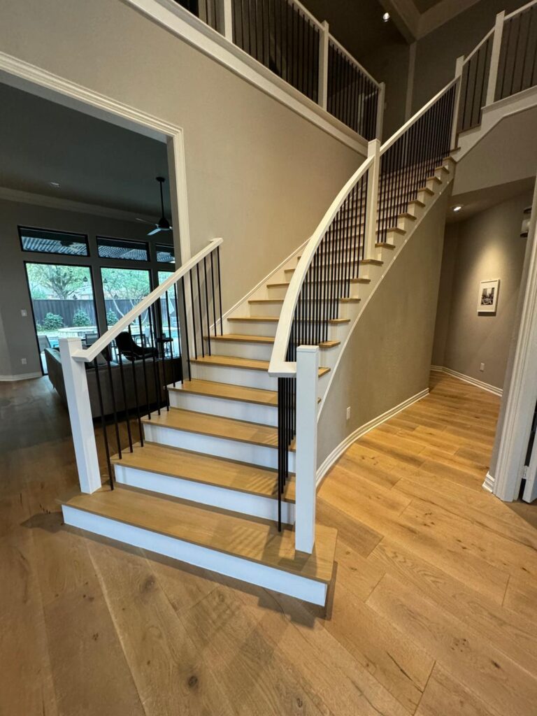 Elegant staircase remodeling in Plano featuring curved design, modern black iron railings, and light wood steps for a contemporary home upgrade.