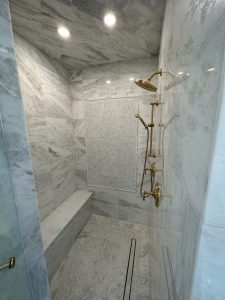 Marble walk-in shower with built-in bench and brass fixtures in a Plano bathroom remodel