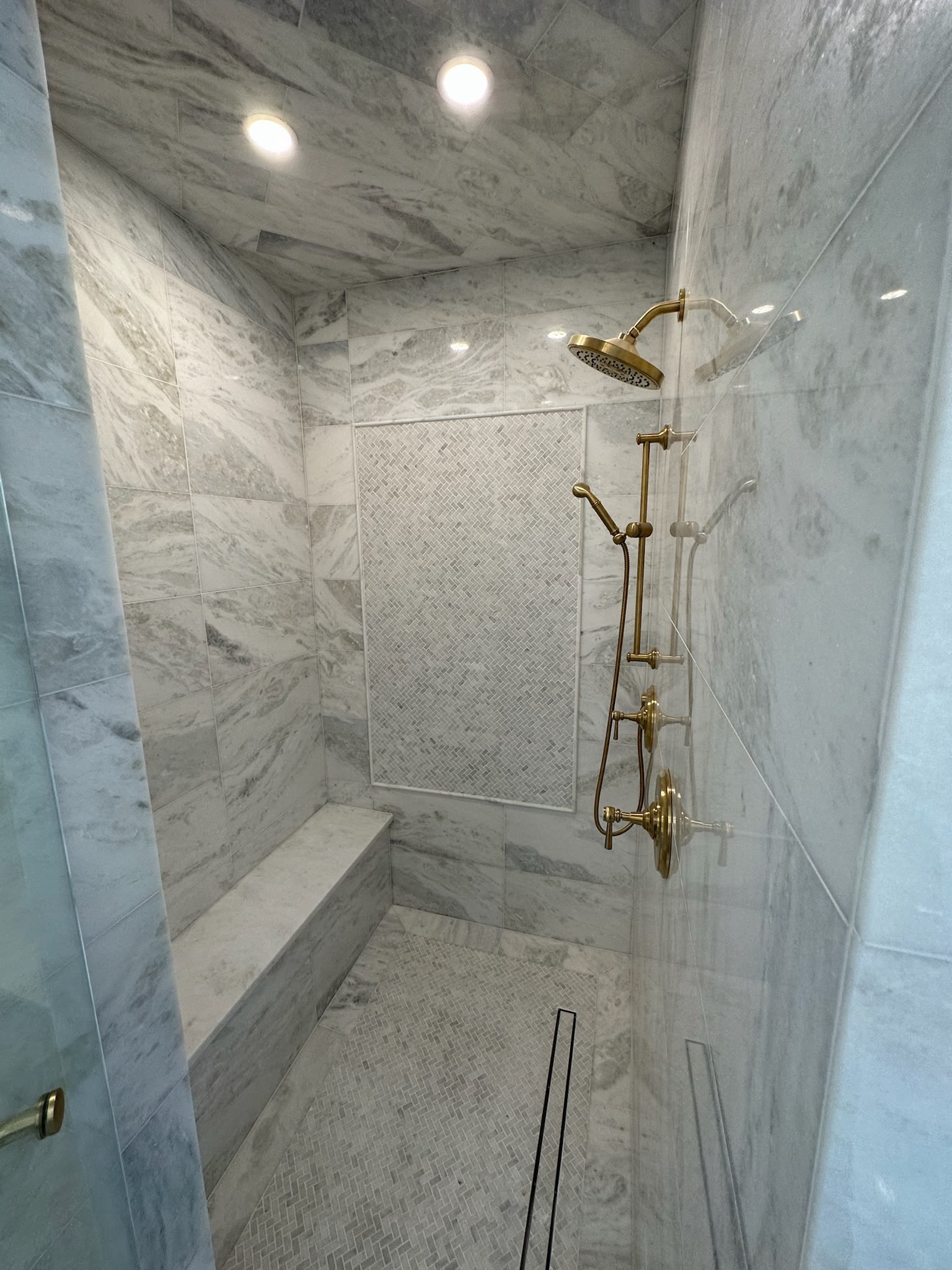 Marble walk-in shower with built-in bench and brass fixtures in a Plano bathroom remodel