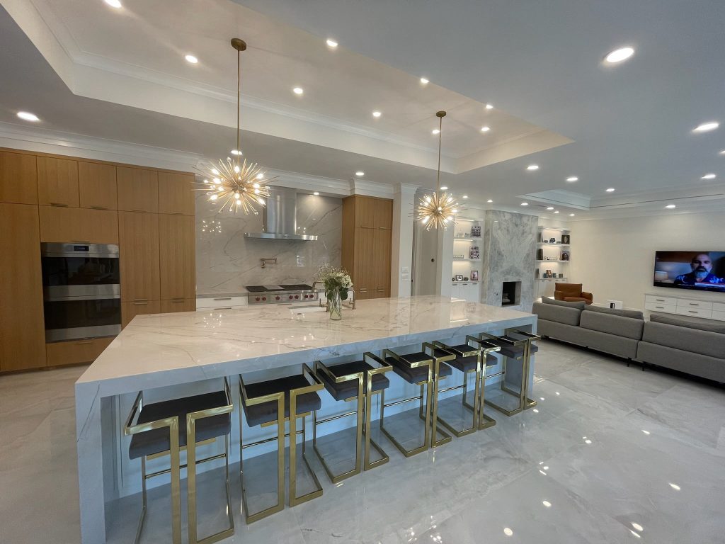 Luxury open-concept kitchen remodel with oversized stone island, wood cabinetry and statement lighting