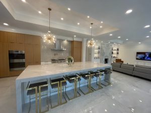 Luxury open-concept kitchen remodel with oversized stone island, wood cabinetry and statement lighting